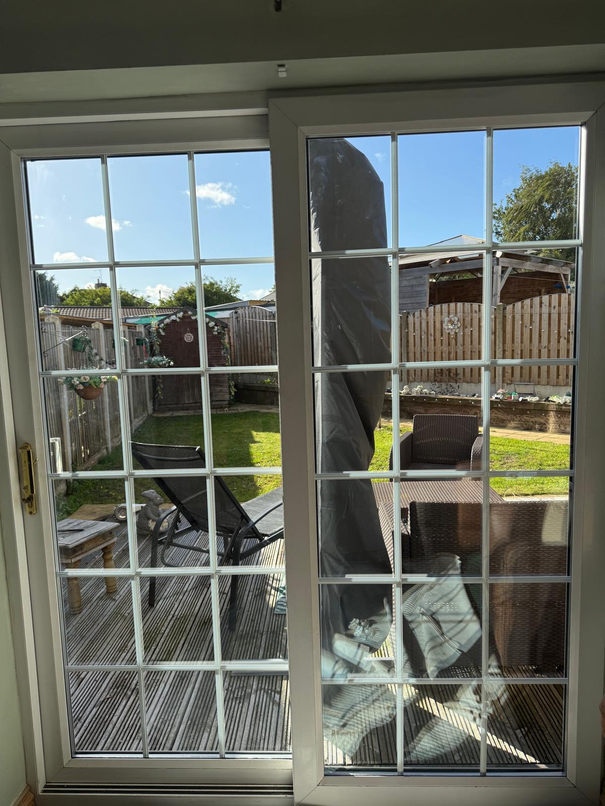 After: the same white uPVC Georgian bar sliding patio doors with new glass, both panes clear and looking out onto a sunny garden