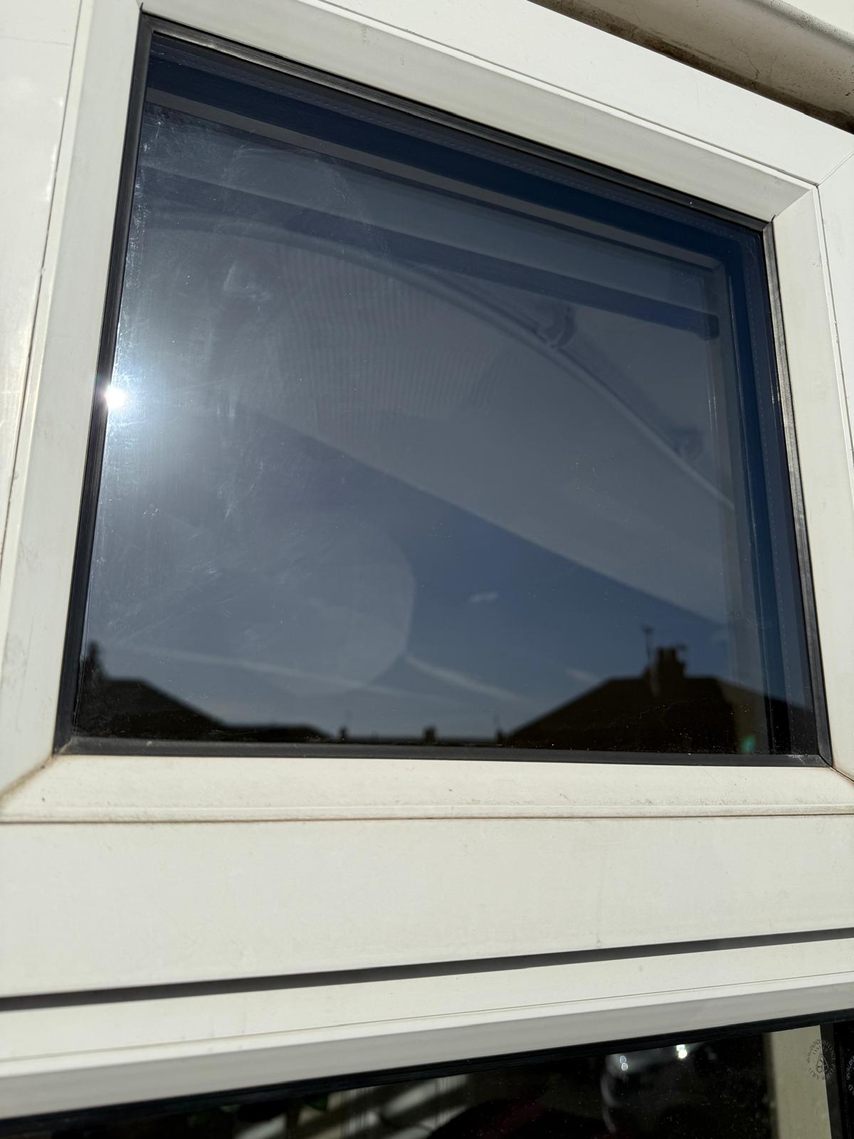 After: the same white uPVC top light window with a new sealed unit, the clear glass reflecting blue sky and rooftops